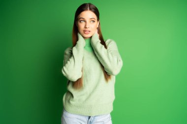 Young teen girl in jumper looking away on green background 