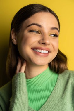 Positive teen girl with makeup looking away on yellow background with shadow 