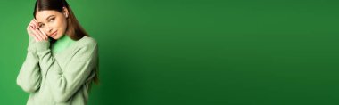 Teenager in cozy sweater looking at camera isolated on green, banner 
