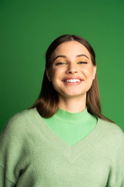 Portrait of happy teen girl in jumper smiling at camera isolated on green 