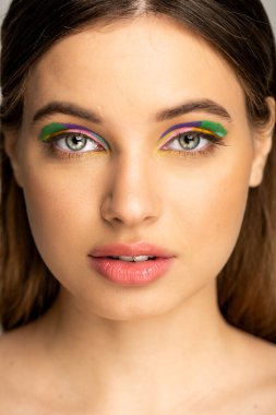Teenage girl with colorful makeup looking at camera isolated on grey 