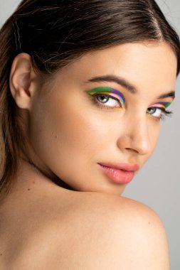 Portrait of teen girl with colorful eyeshadow and naked shoulder looking at camera isolated on grey 