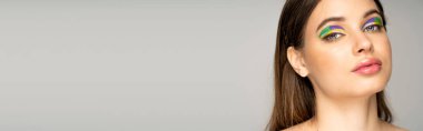 Portrait of teenage girl with colorful visage looking at camera isolated on grey with copy space, banner 