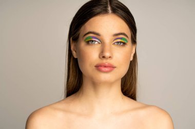 Teenage model with naked shoulders and colorful eyeshadows isolated on grey 