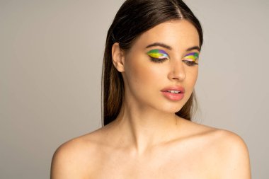 Pretty teen model with colorful visage and naked shoulders posing isolated on grey 