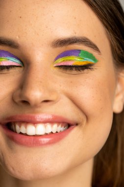 Cropped view of freckled teenage girl with colorful makeup 