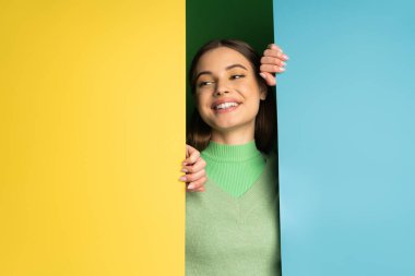 Smiling teen model in soft jumper looking away near colorful background 