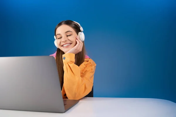 Positive Teen Girl Using Headphones Blurred Laptop Table Isolated Blue — Foto Stock