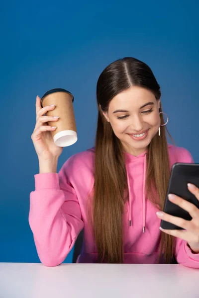 Positive Teen Girl Holding Coffee Using Smartphone Isolated Blue —  Fotos de Stock
