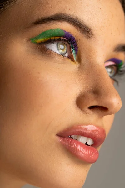 stock image Close up view of teen model with freckles and colorful makeup looking away isolated on grey 