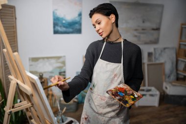 Brunette short haired artist painting on canvas in studio 