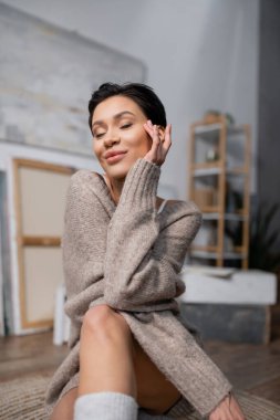 Pleased artist in sweater sitting on floor in studio 