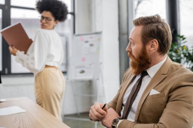 bearded businessman looking at buttocks of displeased african american woman in office 