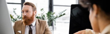 bearded businessman using computer near blurred african american colleague, banner 