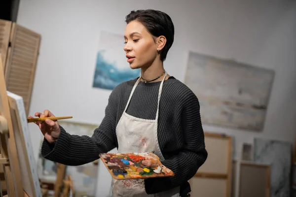 stock image Brunette artist in apron painting on canvas in workshop 