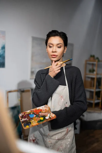 stock image Concentrated artist holding paintbrush and palette in workshop 