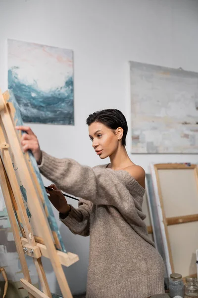 stock image Sexy artist in sweater painting on canvas in workshop 