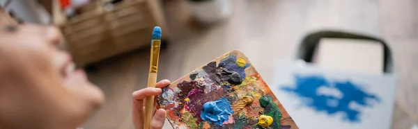 stock image Cropped view of blurred artist holding paintbrush and palette in studio, banner 