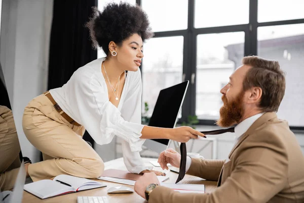 african american businesswoman pulling tie while seducing bearded coworker in office 