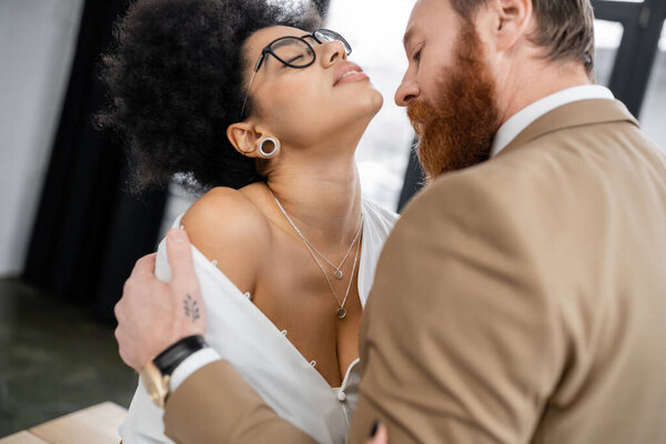 tattooed man undressing seductive african american woman in office 