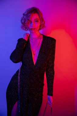 young woman with blonde hair standing in black tight dress and holding chain on purple and pink 