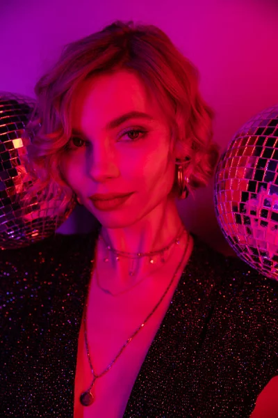 young woman with blonde hair near shiny disco balls on purple and pink 