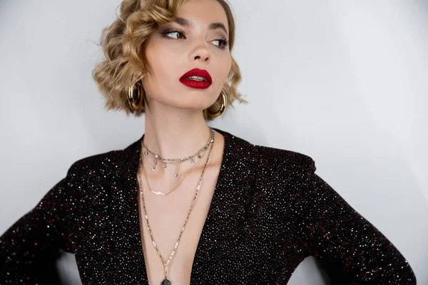 young woman with blonde curly hair and red lips posing on grey 
