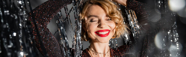 счастливая женщина в блестящем черном платье танцует возле блестящей мишуры занавес на серый, баннер 