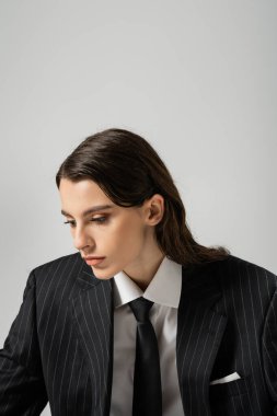 young brunette woman in black blazer and tie posing isolated on grey
