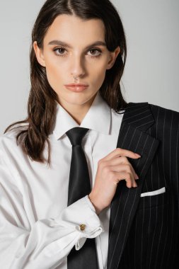 portrait of brunette model in white shirt and tie posing with black blazer isolated on grey