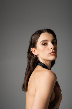 seductive brunette woman hiding breast and looking at camera isolated on grey