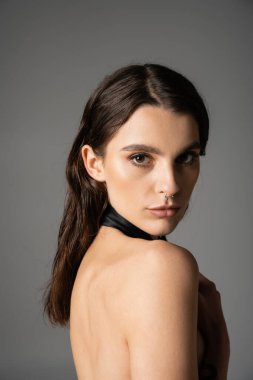 portrait of sensual and shirtless woman with makeup and piercing looking at camera isolated on grey