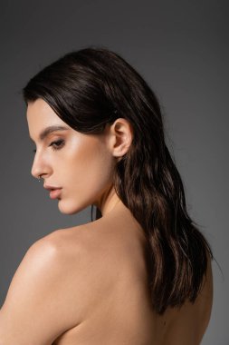 profile of sensual shirtless woman with brunette hair posing isolated on grey