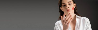 pretty woman with red lipstick mark on face looking at hand on grey background, banner