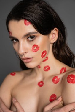 portrait of sexy shirtless woman with red lipstick marks looking at camera isolated on grey