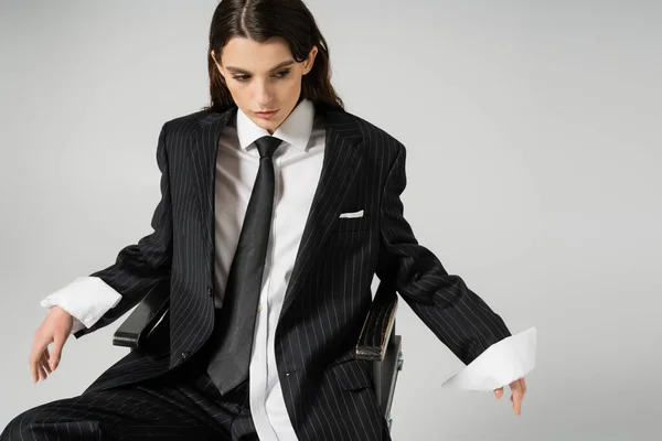 stock image young woman in white oversize shirt and black striped suit sitting on chair isolated on grey