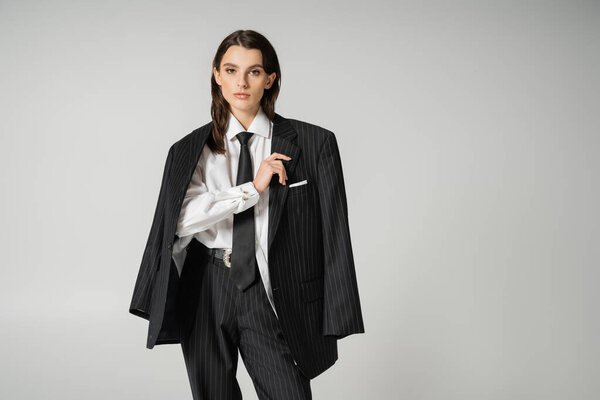 brunette model in white shirt and black trousers with blazer looking at camera isolated on grey