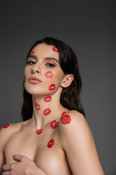 соблазнительная женщина с красными отпечатками губ на лице и бюст без рубашки с рукой, изолированной на сером
