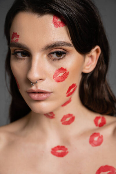 портрет красивой брюнетки с красными отпечатками поцелуев на лице и теле, изолированными на сером