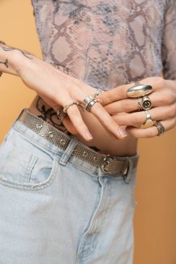 Cropped view of queer person touching rings on fingers isolated on yellow 