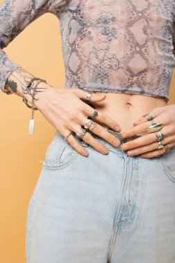 Cropped view of tattooed queer person with accessories isolated on yellow 