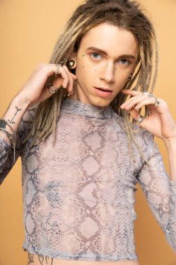 Portrait of tattooed queer person with dreadlocks looking at camera isolated on yellow 