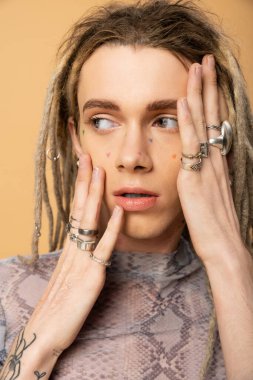 Portrait of tattooed queer person with accessories looking away isolated on yellow 