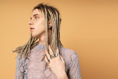 Stylish queer person touching dreadlocks isolated on yellow 