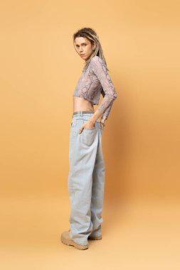 Full length of trendy queer person looking at camera on yellow background 