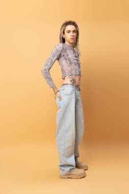 Full length of stylish queer person looking at camera on yellow background 