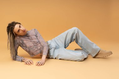 Stylish queer person with dreadlocks looking at camera on yellow background 