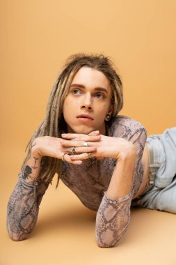 Portrait of tattooed queer person with dreadlocks posing on yellow background 