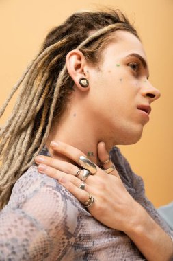 Tattooed nonbinary person with dreadlocks and rings posing isolated on yellow 