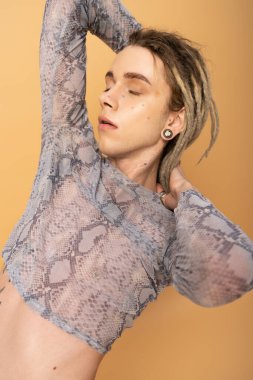 Portrait of tattooed queer person posing in crop top with animal print isolated on yellow 